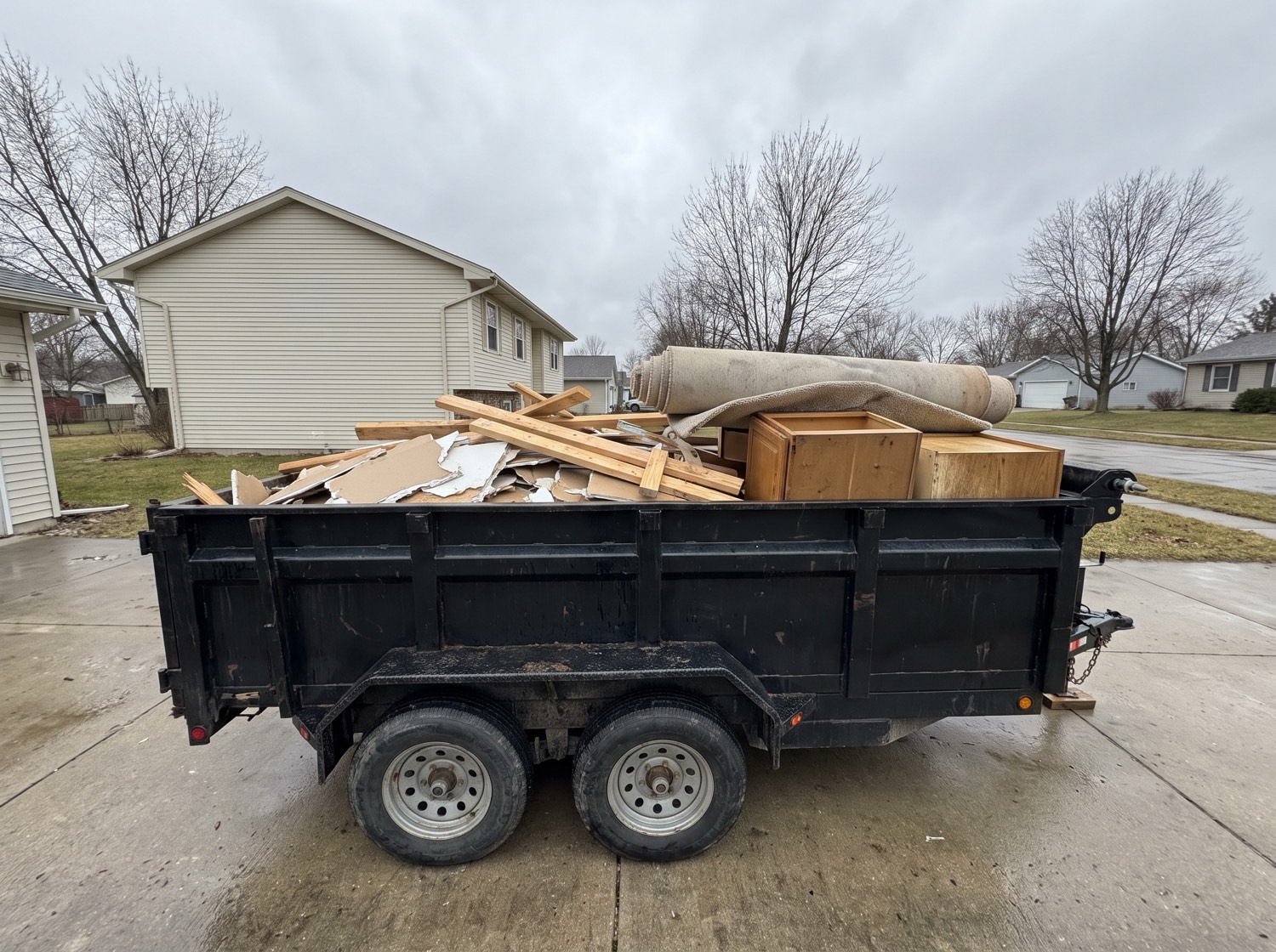 A dump trailer loaded with drywall, lumber, cabinets and old carpet parked on a suburban driveway
