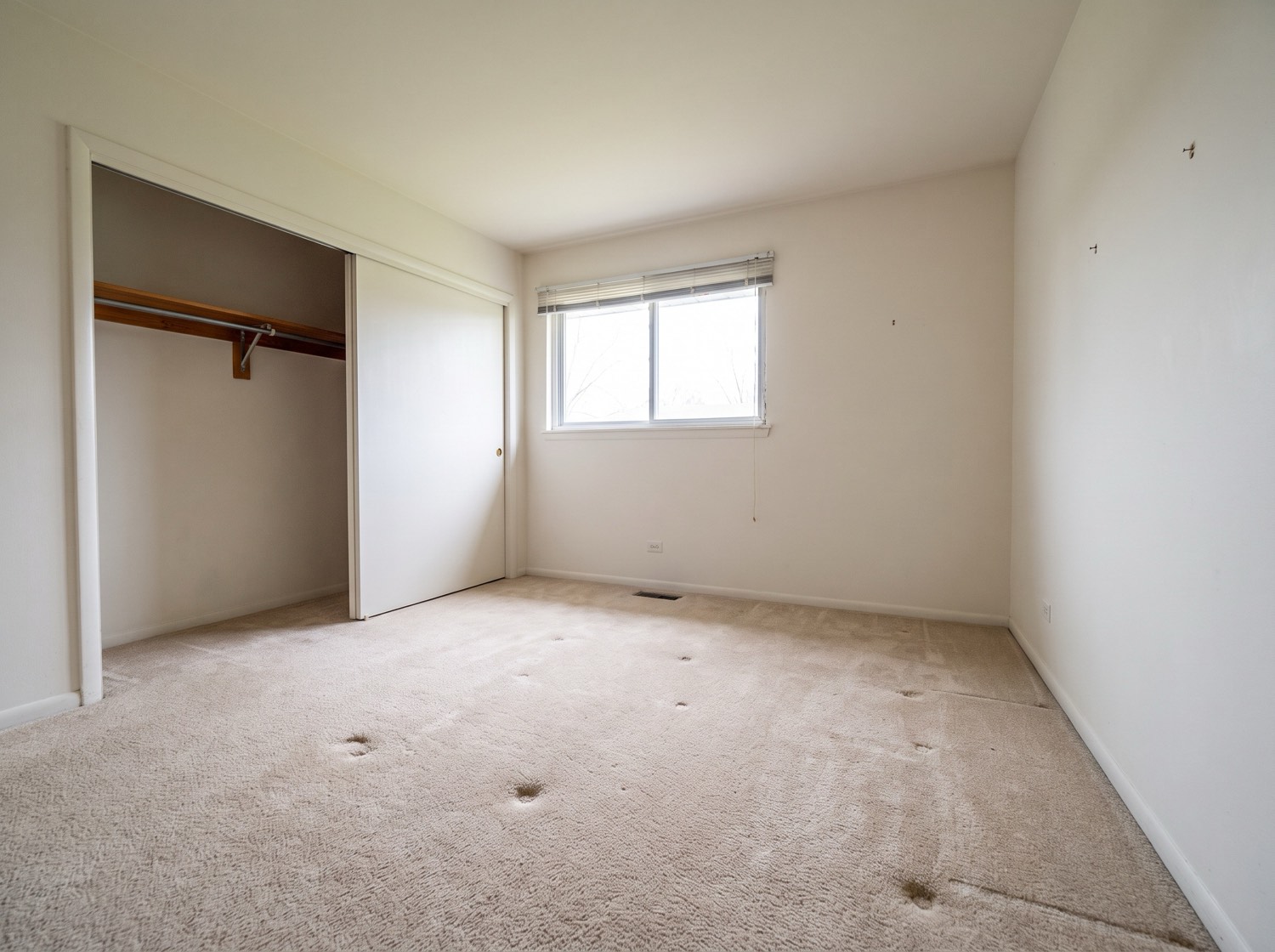 An emptied bedroom in a single-story ranch home, carpet indentations where furniture stood and an empty closet